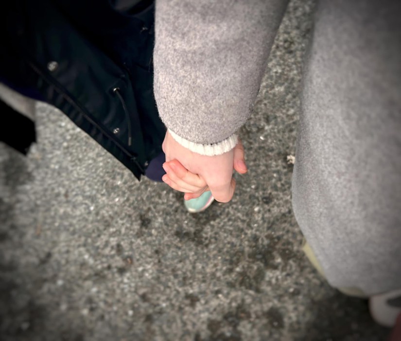 Photo image of a mum holding the hand of her child as they walk down the road.